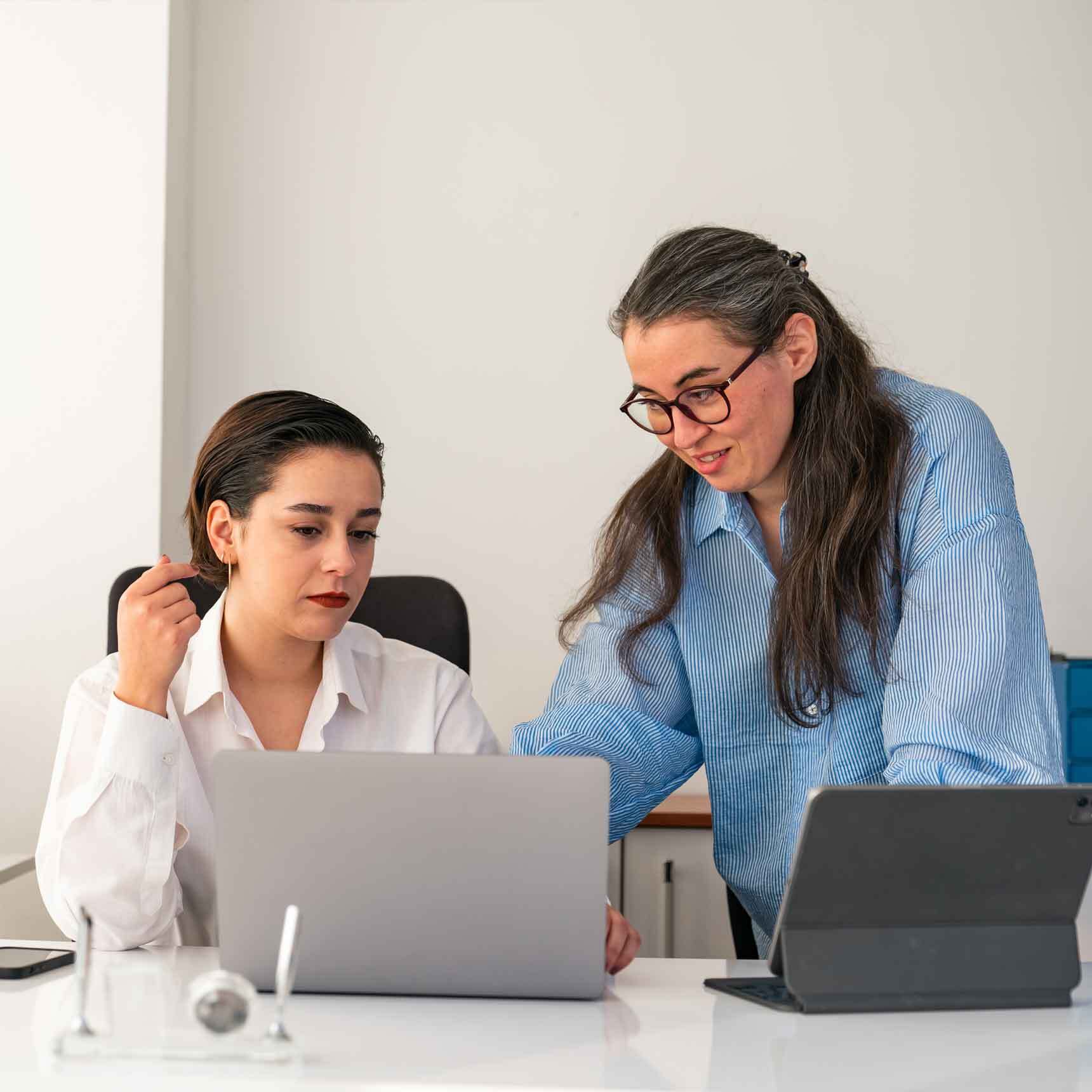 Image depicts two colleagues working together on a computer in an office environment