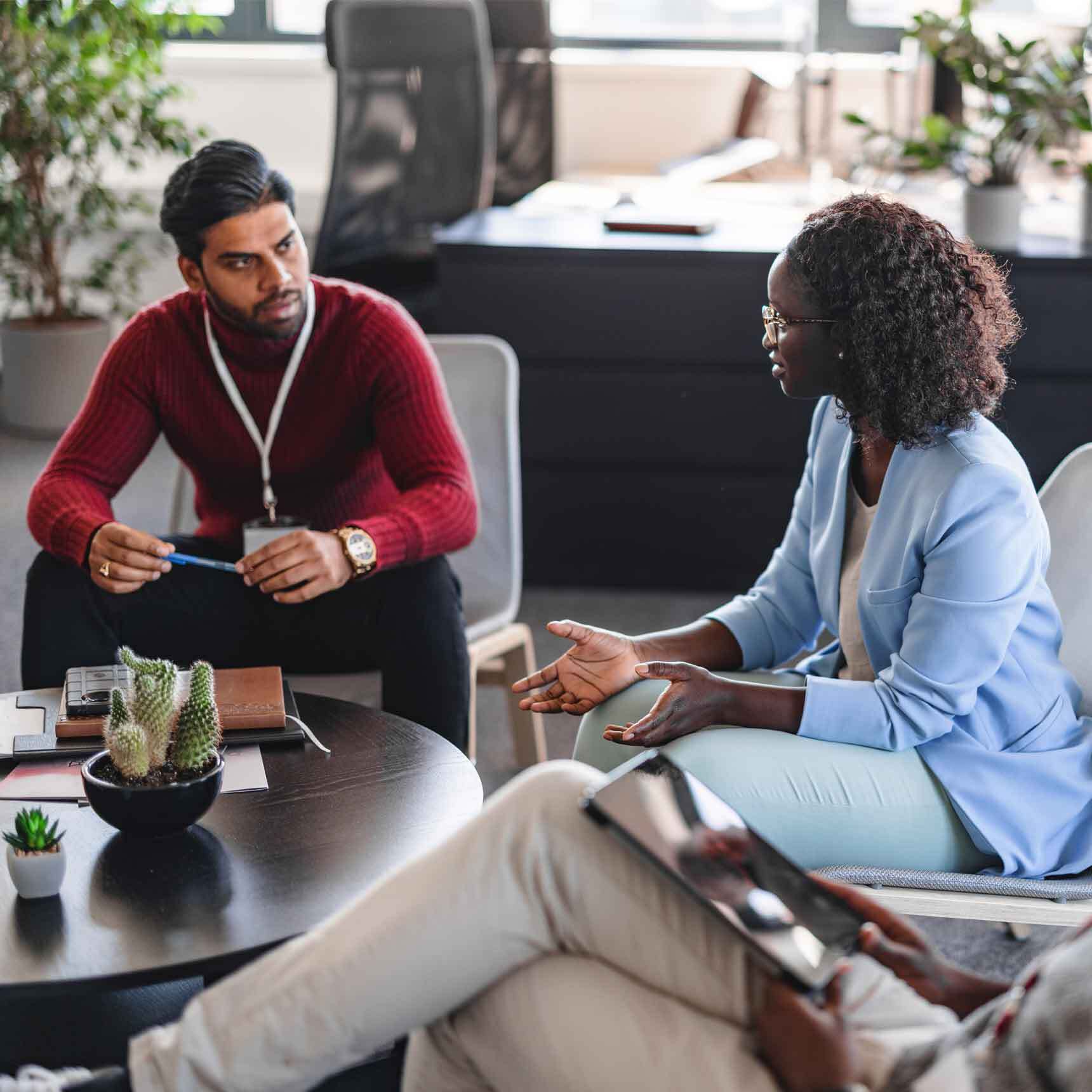 Image depicts a diverse group of individuals gathered around a table, engrossed in a discussion while using a laptop