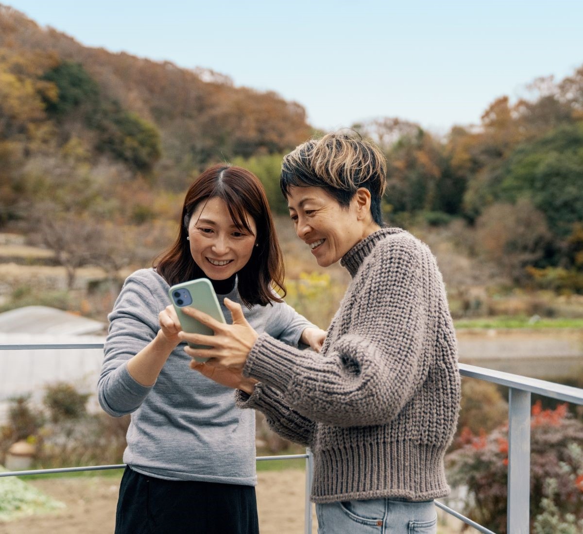 Two women standing on a bridge, focused on a phone, enjoying a moment of connection and modern technology