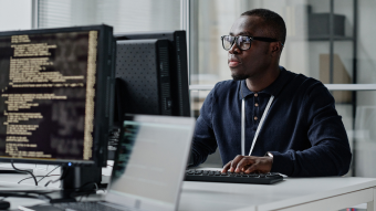 Person with glasses sitting in front of desktop typing 