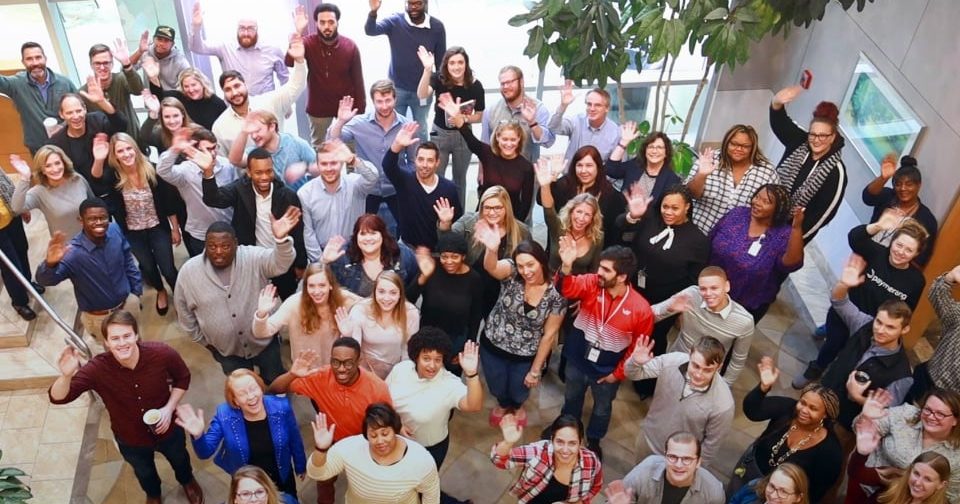 Paymerang employees photographed from above, waving at the camera and smiling.