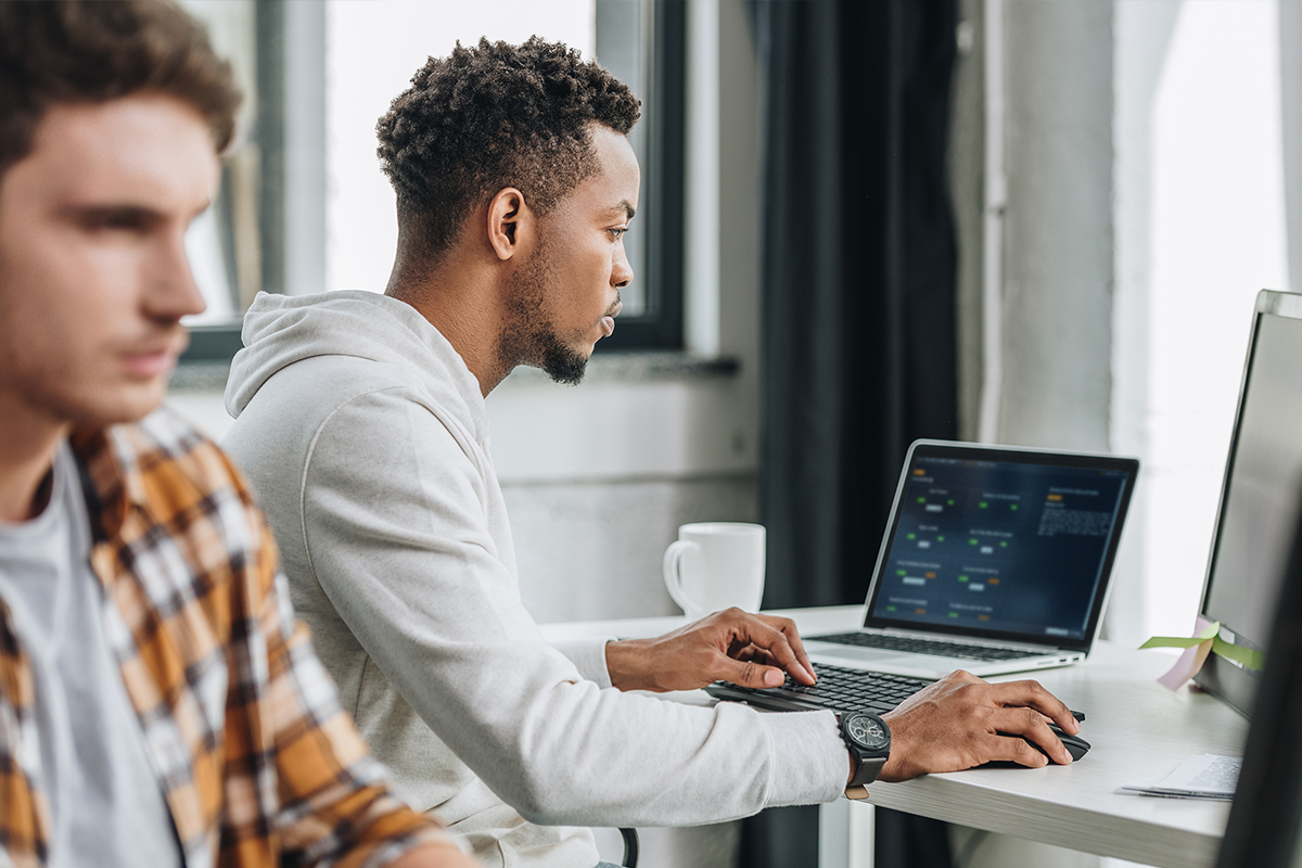 Black man in white shirt seated at a table looking at AWS Jam Journey on laptop screen