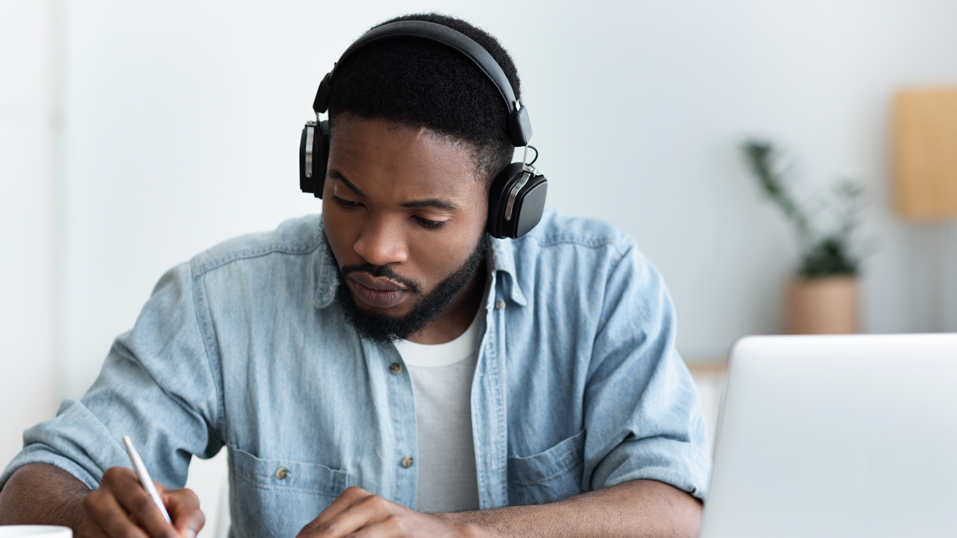 Un hombre con auriculares sentado en un escritorio con un port&aacute;til aprendiendo los aspectos fundamentales y las pr&aacute;cticas recomendadas en la nube de AWS