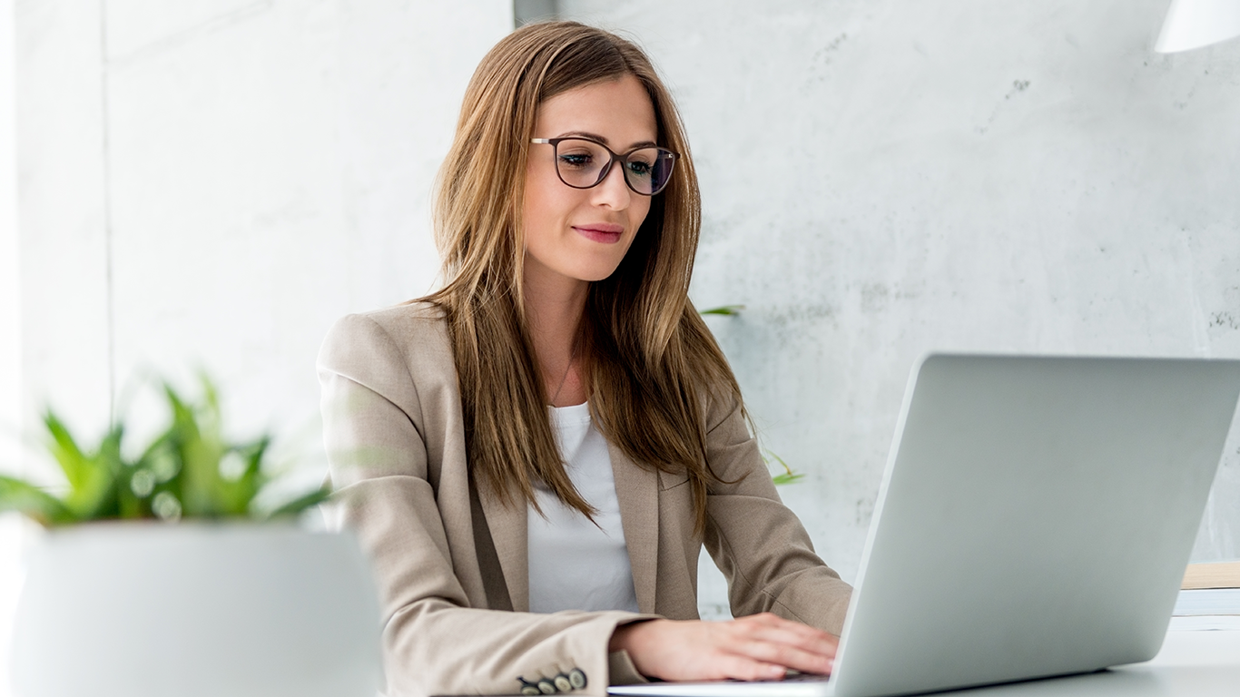 Una mujer que lleva gafas est&aacute; sentada en un escritorio con una computadora port&aacute;til y aprende a mapear el an&aacute;lisis de datos en AWS