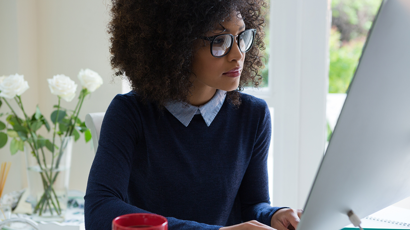 Woman wearing eyeglasses is sitting at a desk with a desktop computer learning how to design and manage AWS database services