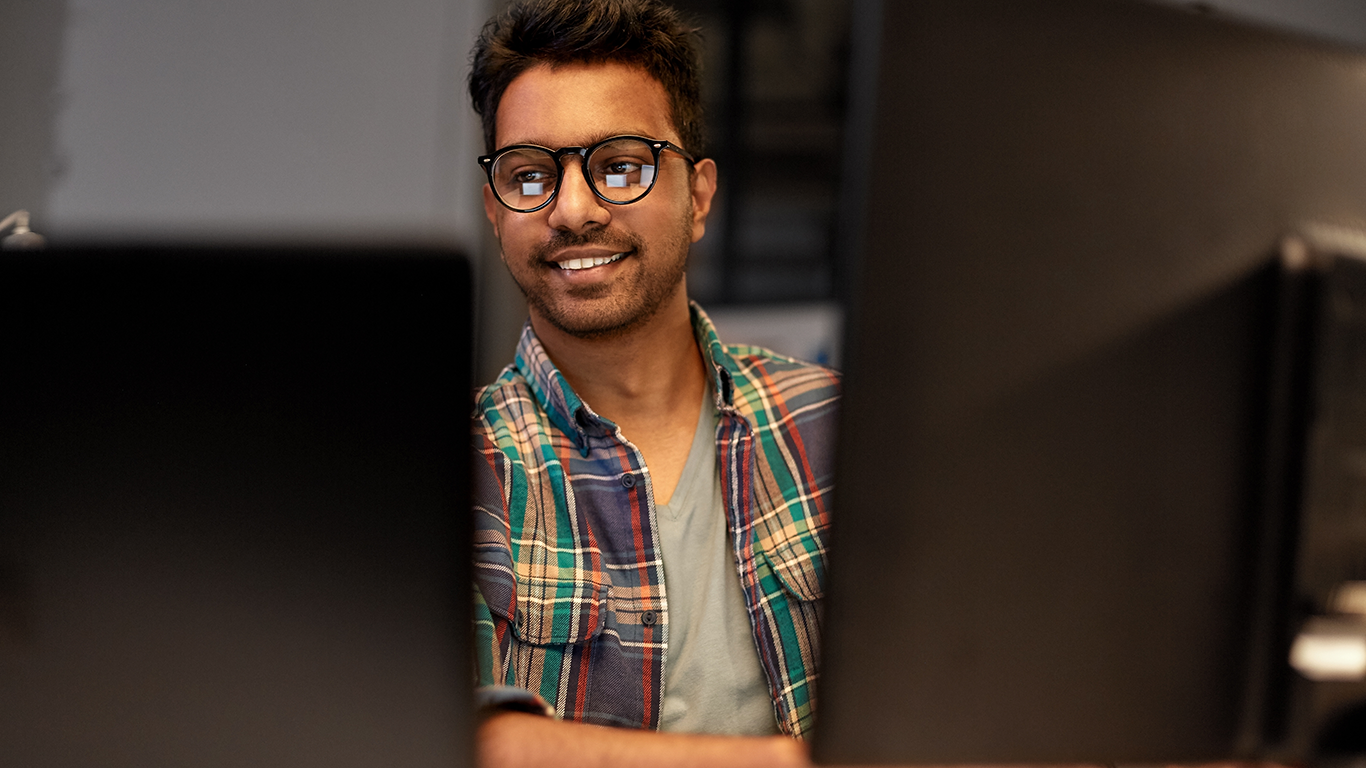 Man sitting at a desk with two desktop monitors learning how to develop, host, and scale multiplayer games.