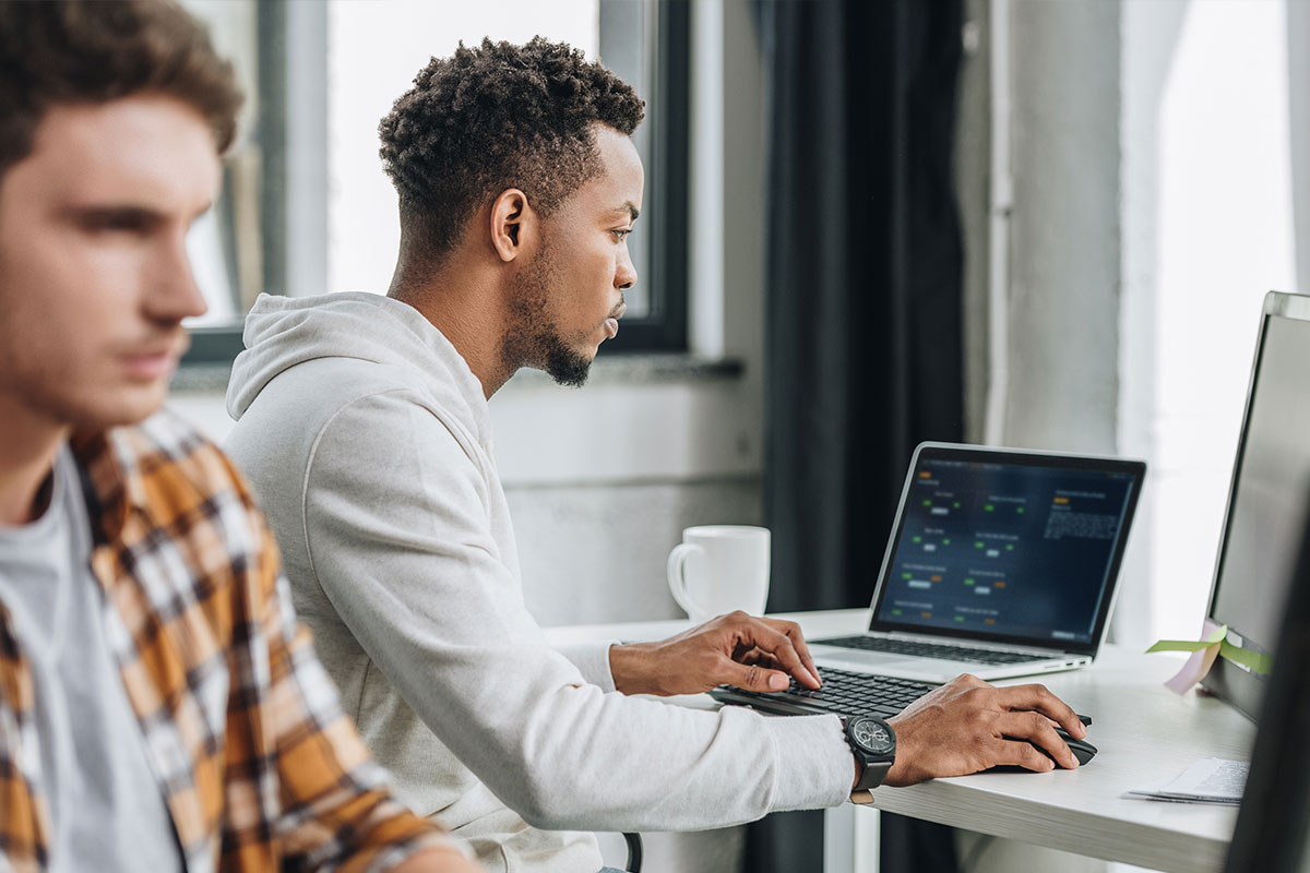 Zwei Männer sitzen am Tisch und spielen AWS Jam auf Laptops