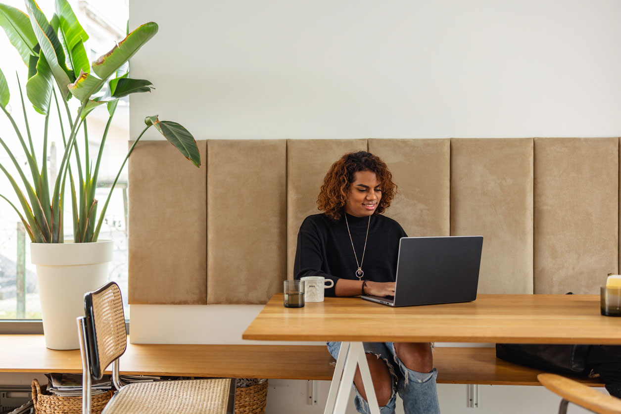 Una donna nera seduta a un tavolo che segue un corso di preparazione agli esami sul laptop