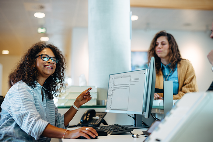 Woman working at government office reception looking away and smiling with people standing in queue at front desk.